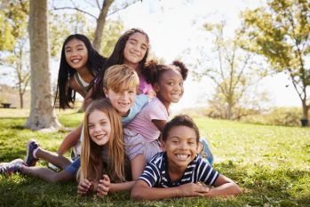 Multi-ethnic group of kids lying on each other in a park diverse group of children lying on each other in a park