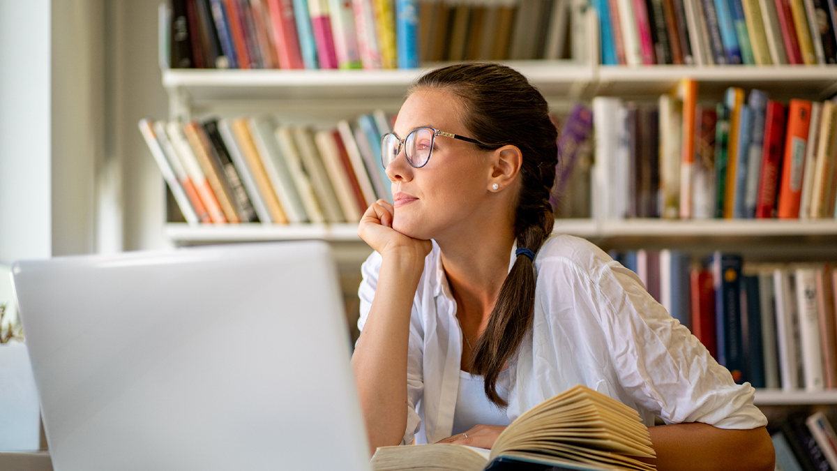 -- title missing -- Young woman seated at desk in home office with laptop starring outside.