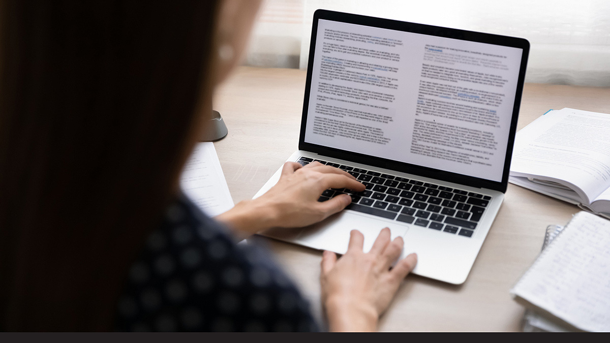 Reading research article Over-the-shoulder photo of young business woman concentrating on electronic documents via laptop.