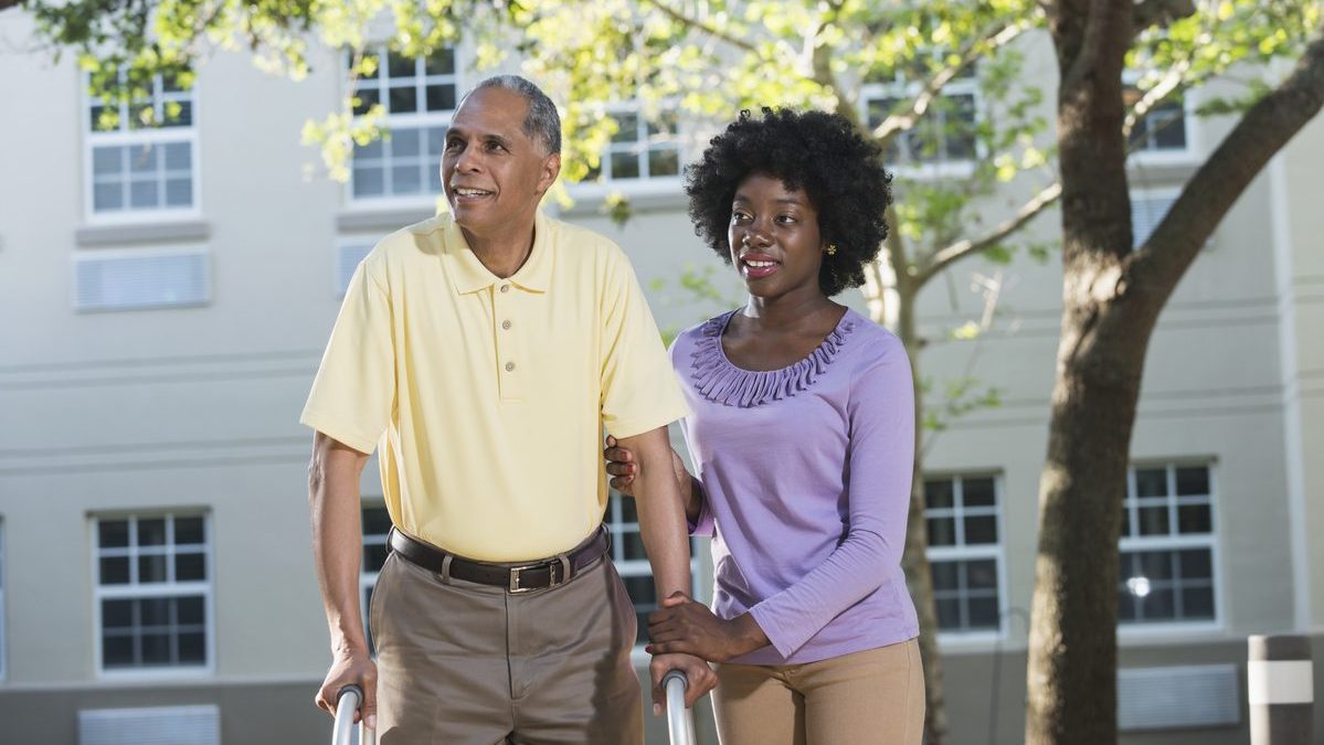 African American woman helping her father with walker Daughter helping father who's using a walker.