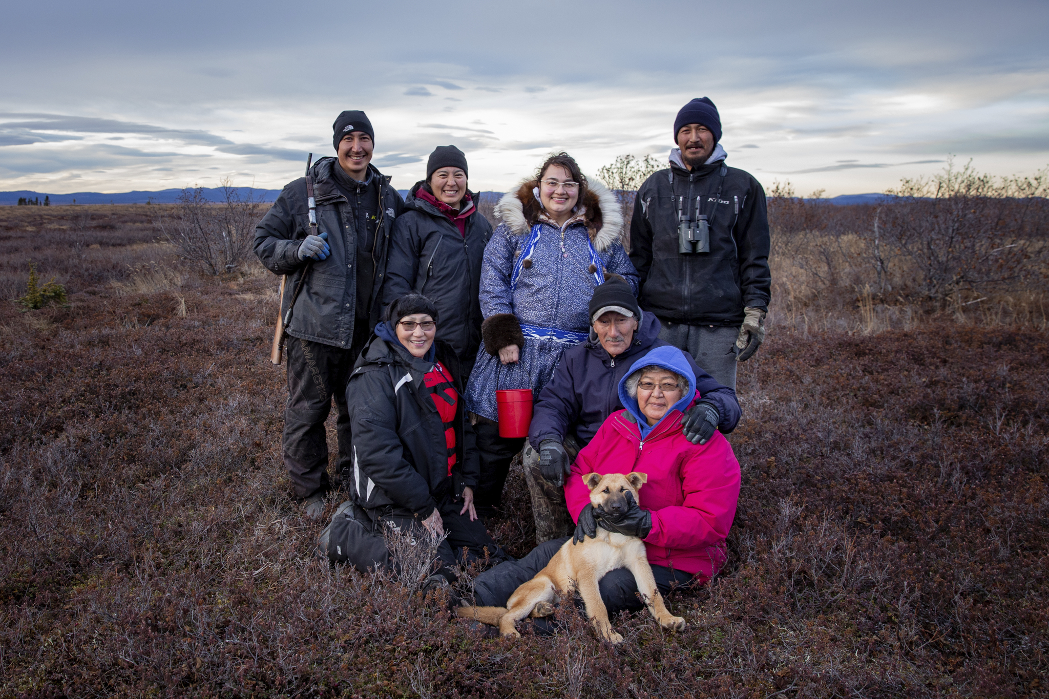 A family of seven smiling people and their dog standing outside.