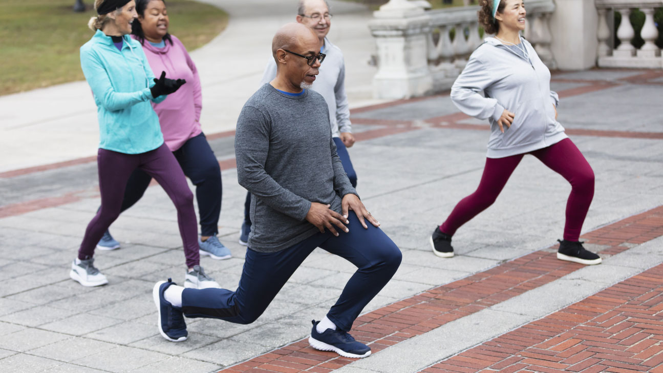 Five adults exercising in park doing lunges Diverse group of middle-age and older adults stretching in the park