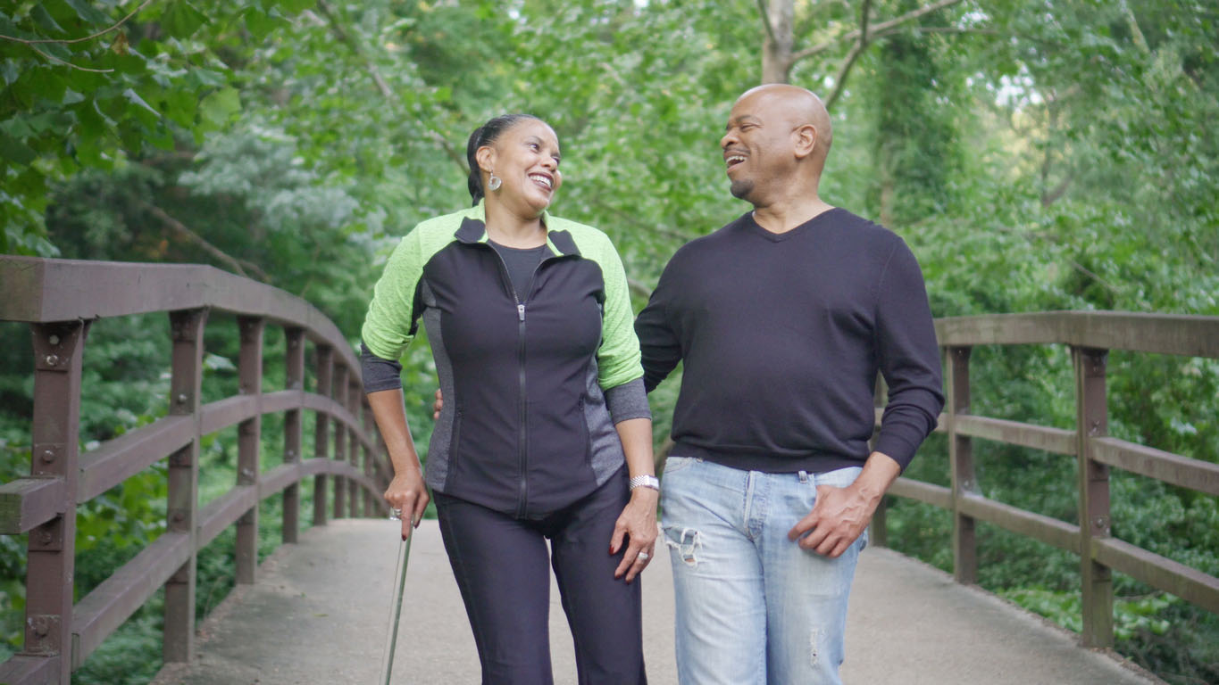Woman walking with cane and talking with man while enjoying nature together Woman walking with a cane and talking to man while crossing a bridge.