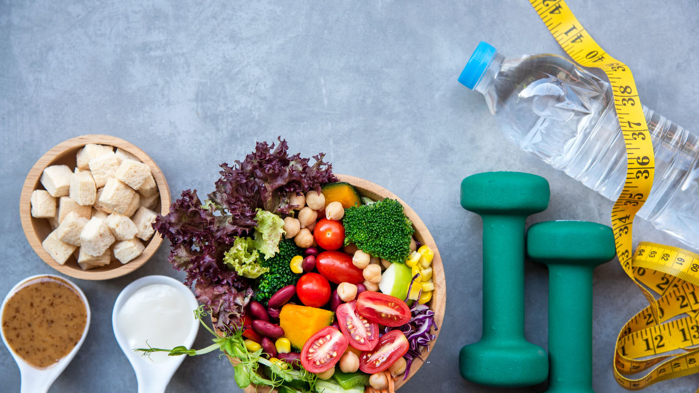 Fresh vegetable salad with dumbbells and water bottle Healthy foods and dumbbells for exercising