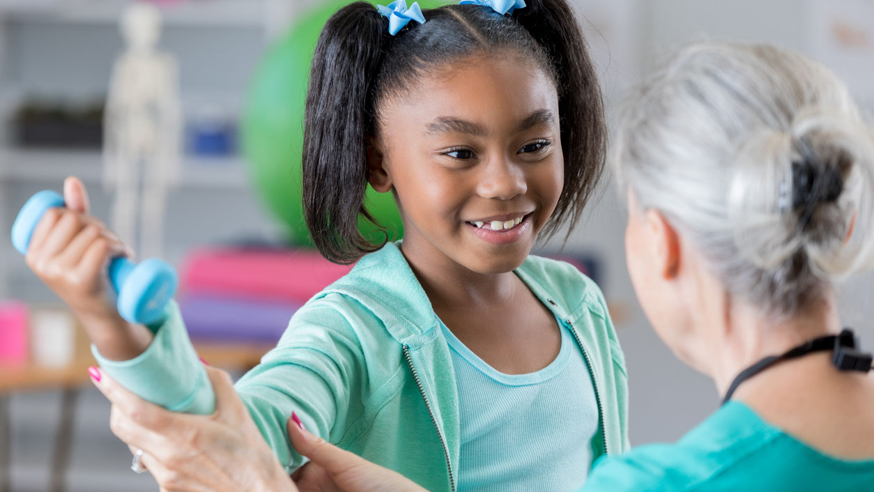 Confident girl in physical therapy session Young child with arthritis lifting dumbbells during physical therapy.