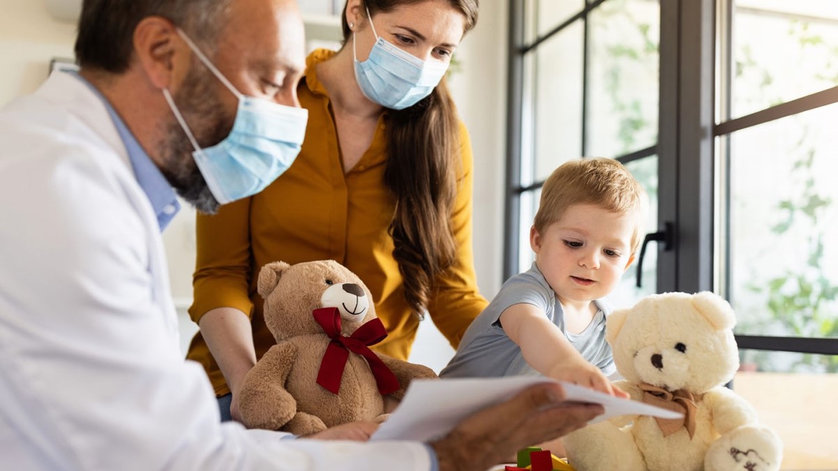 Doctor and parent look on while young patient points at a milestone checklist.
