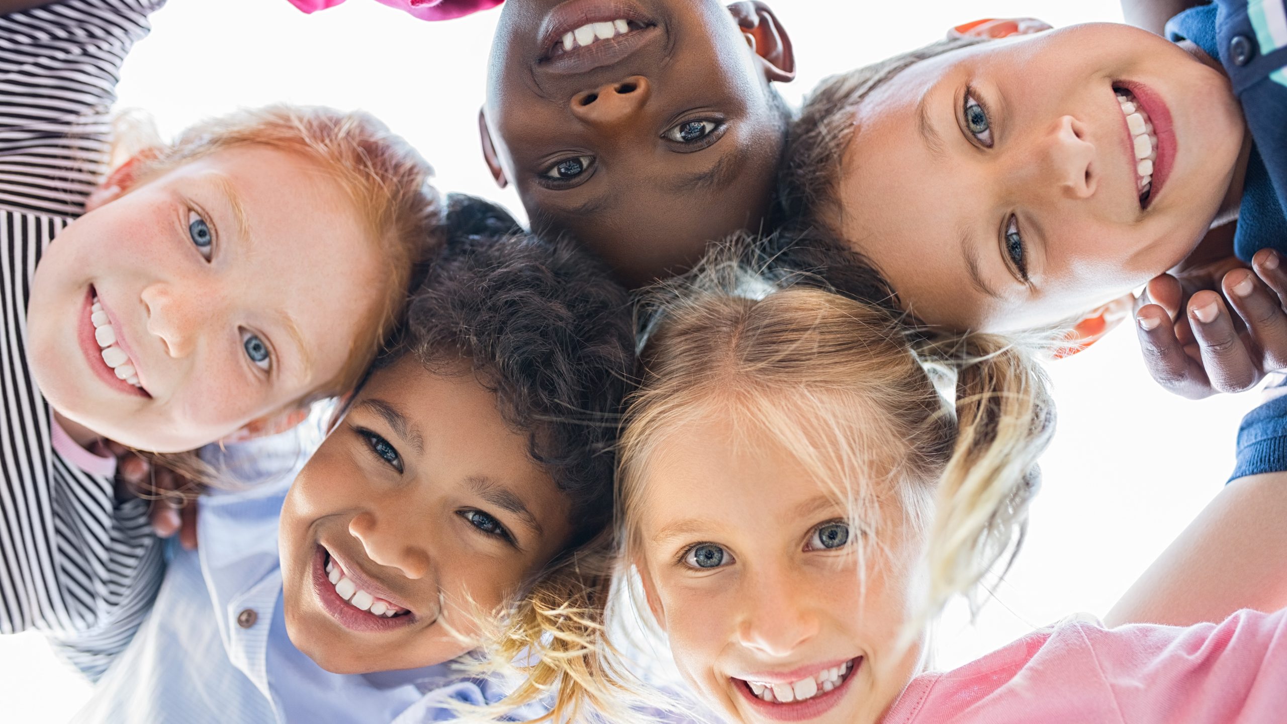 Five young children in a circle smiling happily down toward camera.