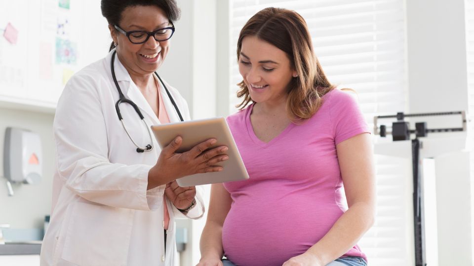 Pregnant woman and doctor smiling Pregnant woman and doctor smiling, looking at a tablet in a healthcare office.