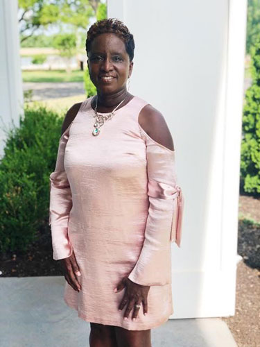 Ena Wanliss standing with her hands to her side while wearing a pink dress