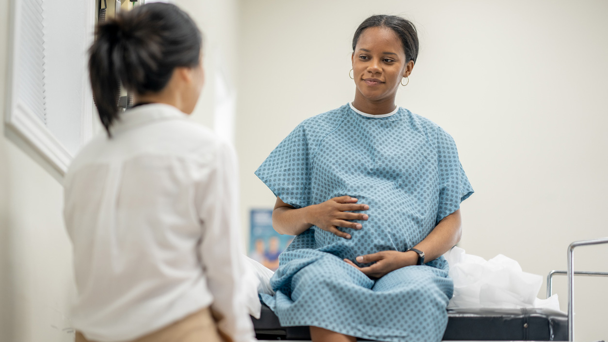 Infant Feeding Practices Study II A pregnant woman, wearing a medical gown, sits on an exam table at a prenatal check-up. A doctor sits across from her.