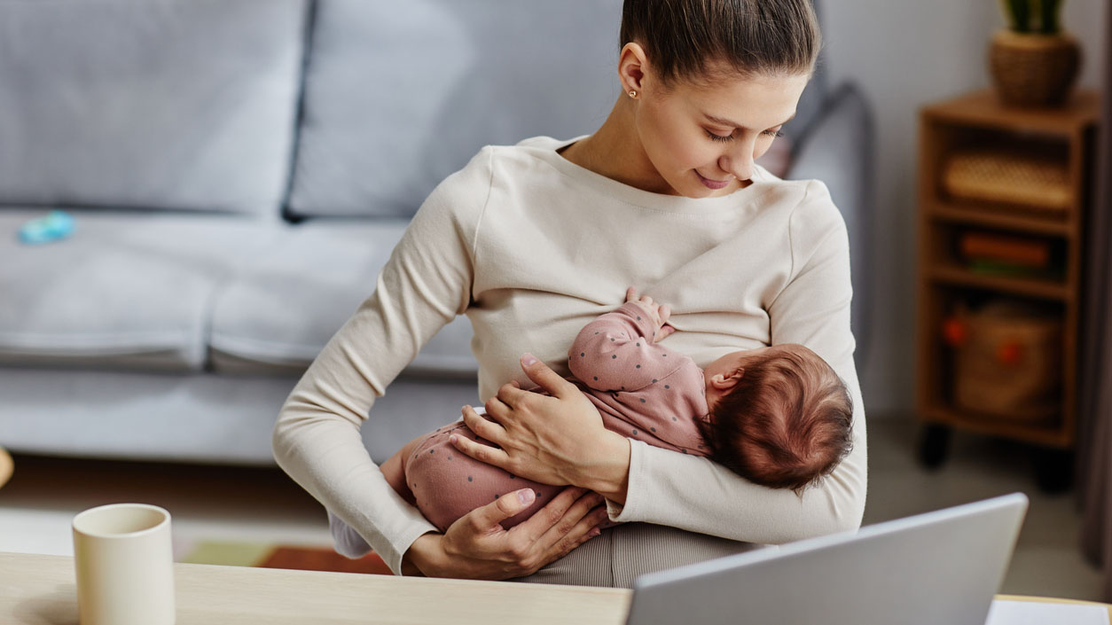 Mom breastfeeding baby A mom breastfeeds her baby in front of desk with a laptop on it.