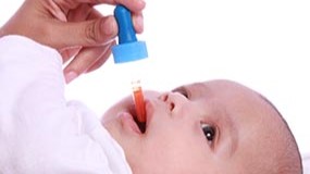 — title missing — A mother using a dropper to give a baby a vitamin supplement.