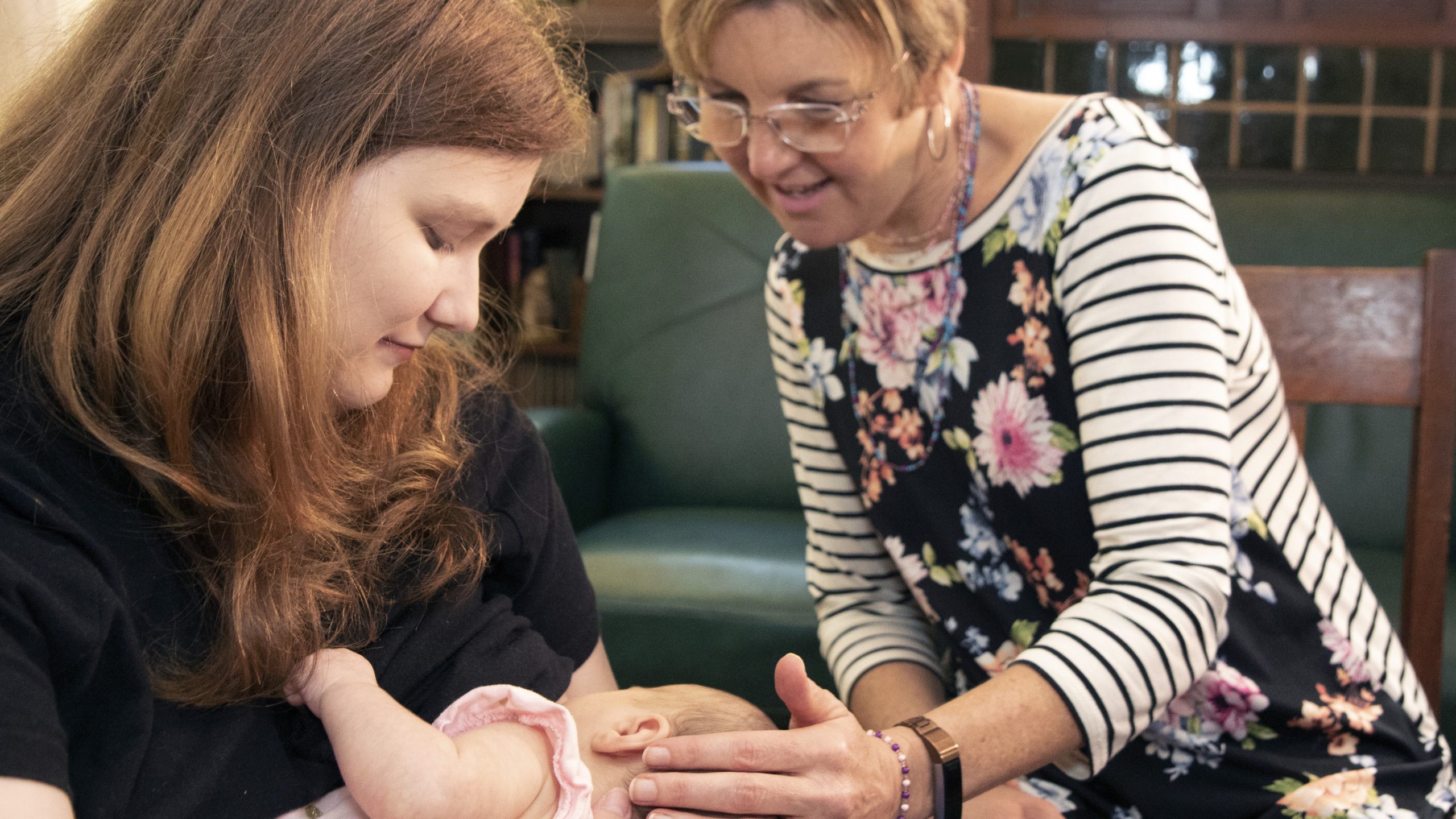 — title missing — A mother breastfeeds her infant with support from an older woman.