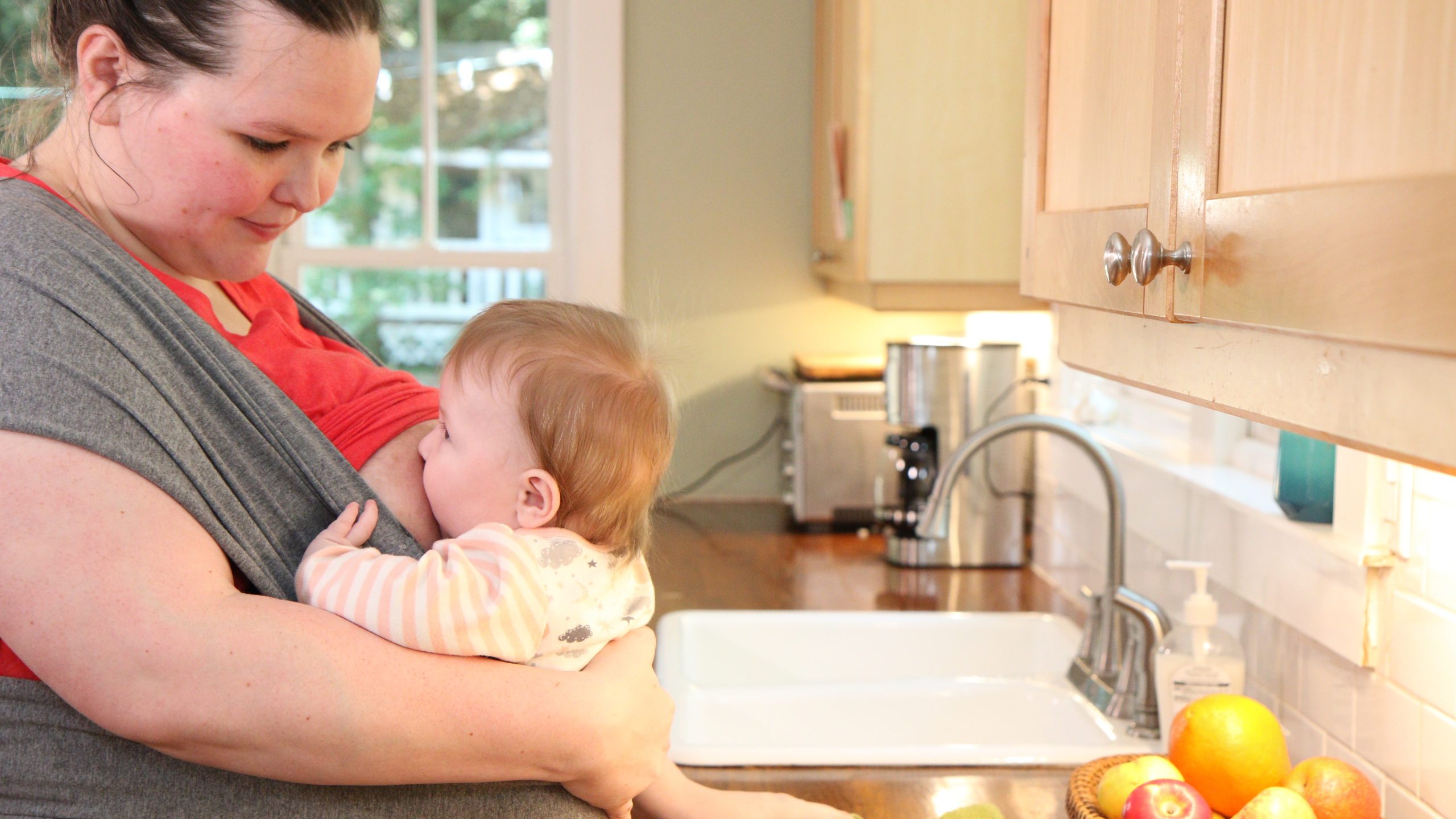 Woman breastfeeds at kitchen counter Woman breastfeeds while standing at the kitchen counter.