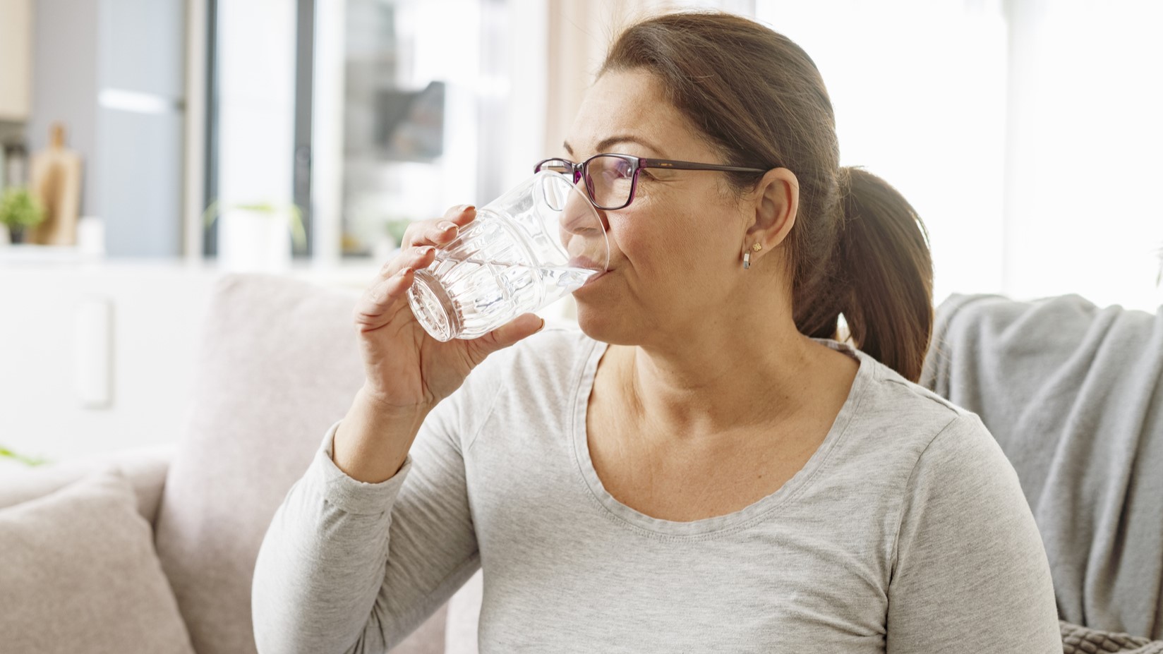 Water An older adult sitting on a couch drinking a glass of water.
