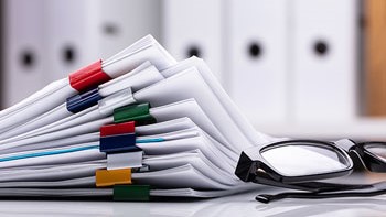 Materials and Resources Stack of papers on a desk next to a pair of glasses.