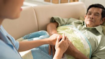 Caregiver and a patient Caregiver holding the hands of a male patient lying on a sofa.