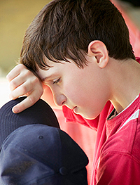 image.png Young boy, holding a cap and wiping his brow.