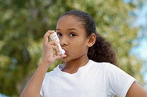 image.png A young girl in a white T-shirt using an inhaler outside.