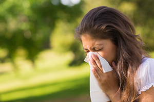 image.png A woman outside blowing her nose into a tissue.