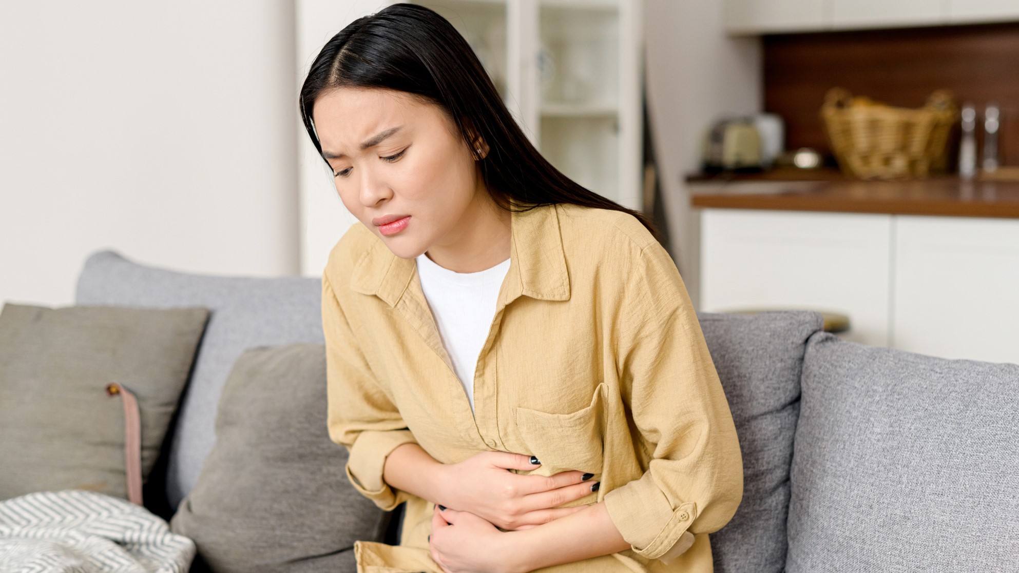 Woman at home on couch, holding stomach in pain