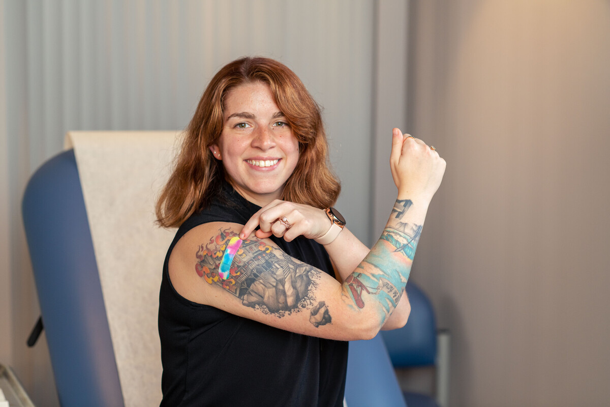 Benefits of vaccination Young woman showing off her recent COVID vaccine and Band-Aid on tattooed upper arm.