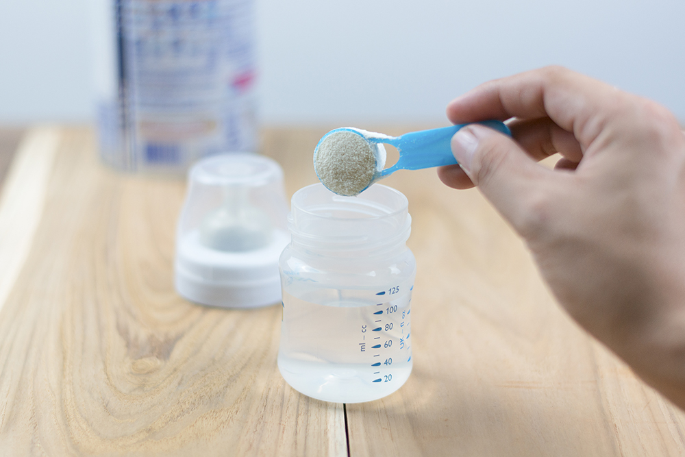Powder milk and blue spoon on light background close-up. Milk powder for baby in measuring spoon on can. Powdered milk with spoon for baby. Baby Milk Formula and Baby Bottles. Powder milk and blue spoon on light background close-up.