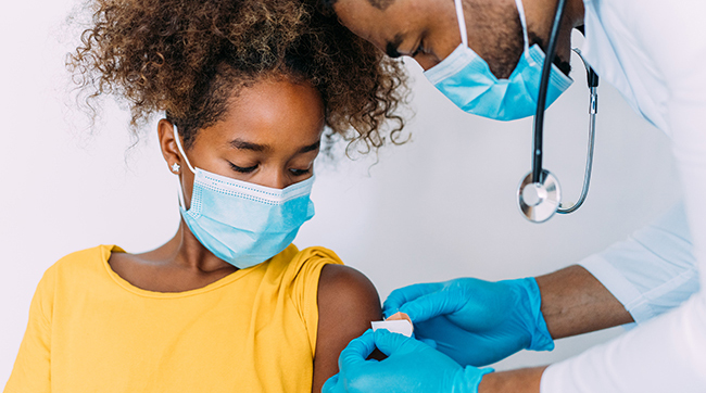 vaccine-girl-slider Proveedor de atención médica aplicando una curita al brazo de una niña.