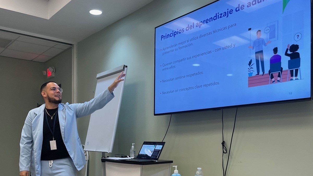 A person standing up presenting using a presentation projected on a TV screen.