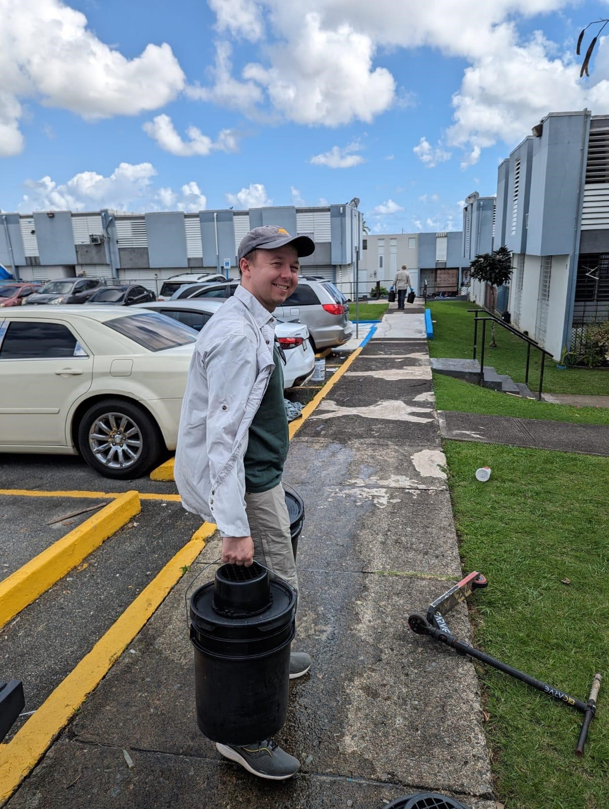 CDC Staff Member Carries AGO Traps A person outside in an apartment complex looking back at the camera and smiling while carrying AGO traps.