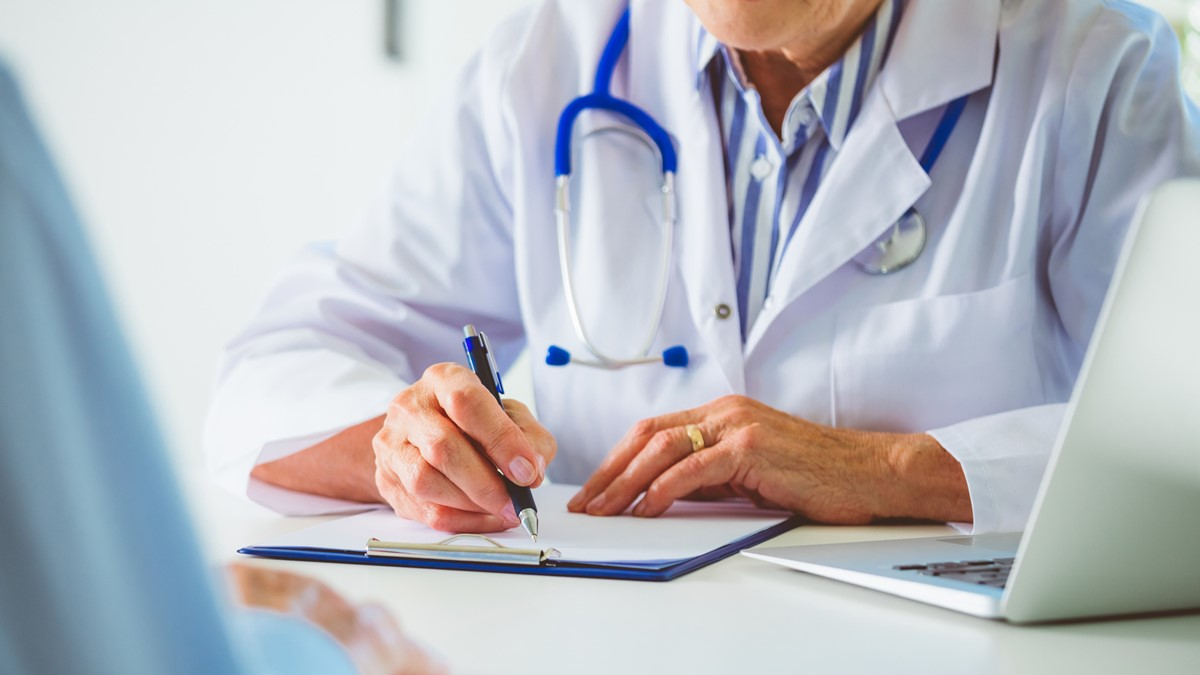 Dengvaxia checklist thumbnail A healthcare provider writing on a clipboard across the desk from patient.