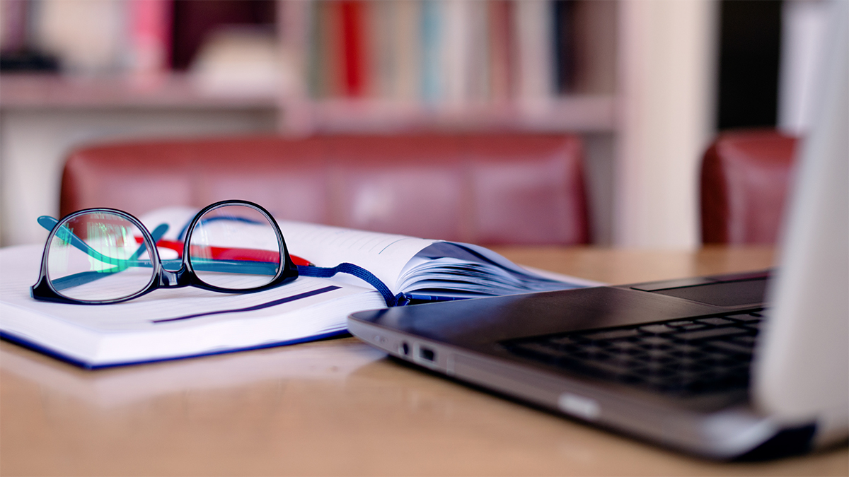 Publications Glasses and notebook next to a laptop