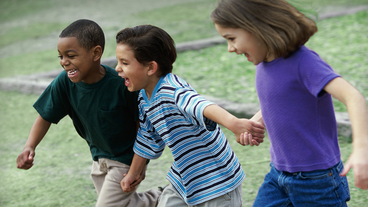 — title missing — Three children holding hands and running in a field.