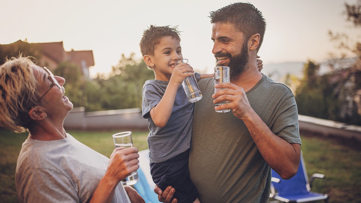 Family drinking water in backyard Family of two adults and one child laughing and drinking water out of glasses in the backyard