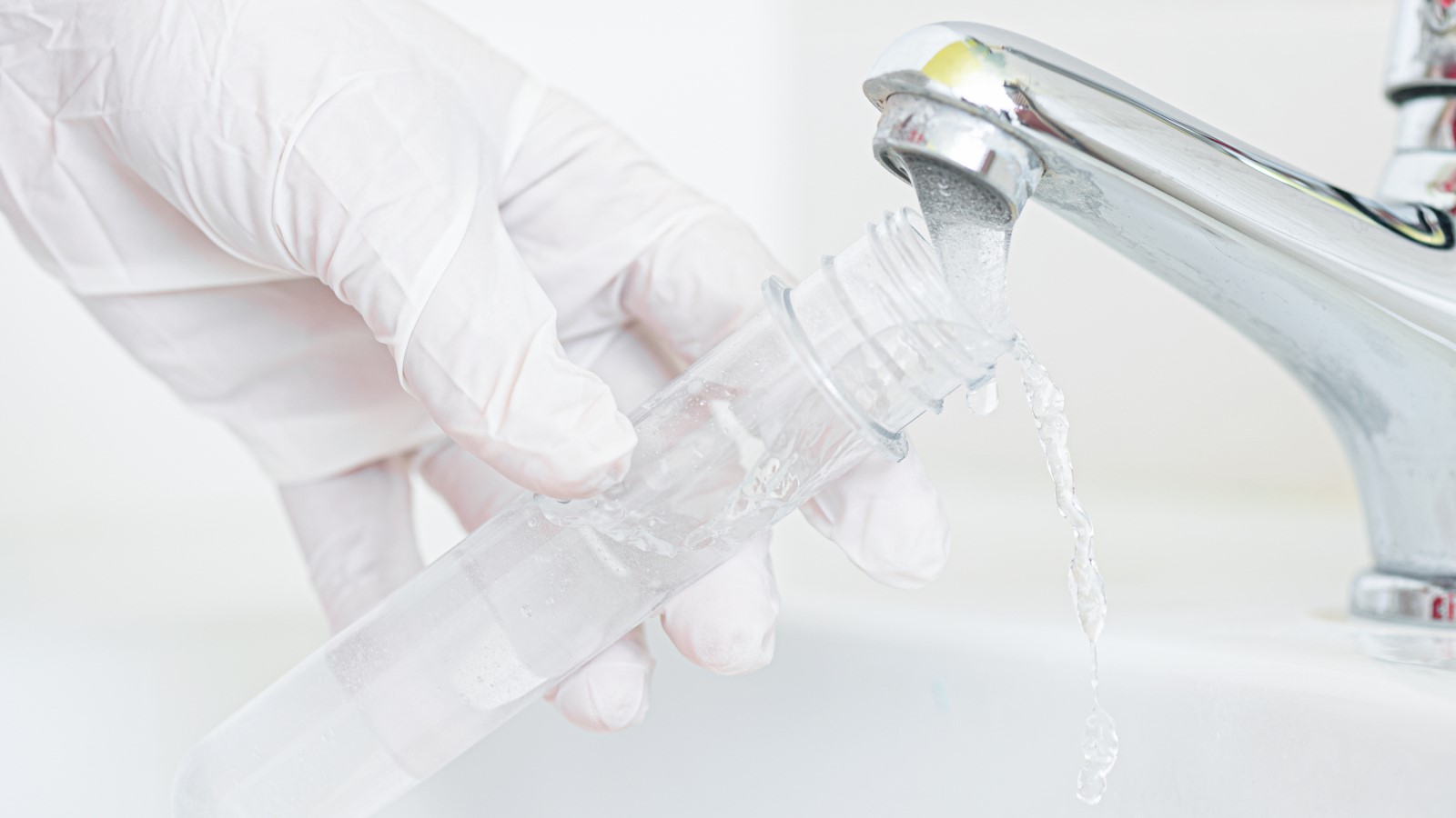 Water testing Gloved hand holding a test tube under a running faucet to collet water