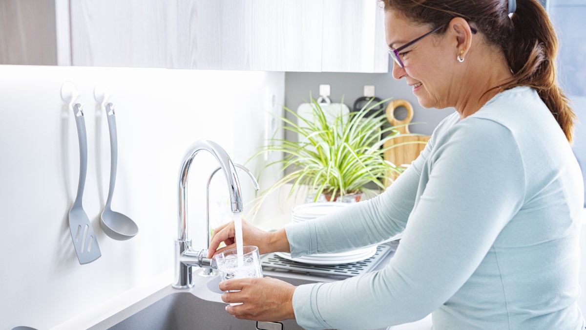 Filling a glass from the tap Smiling woman filling a drinking glass from the water tap in her kitchen