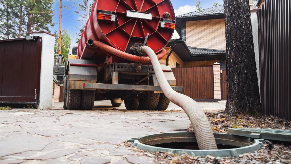 Septic system pumping Large truck with a pipe extending out of its holding tank into a septic system access opening in the ground