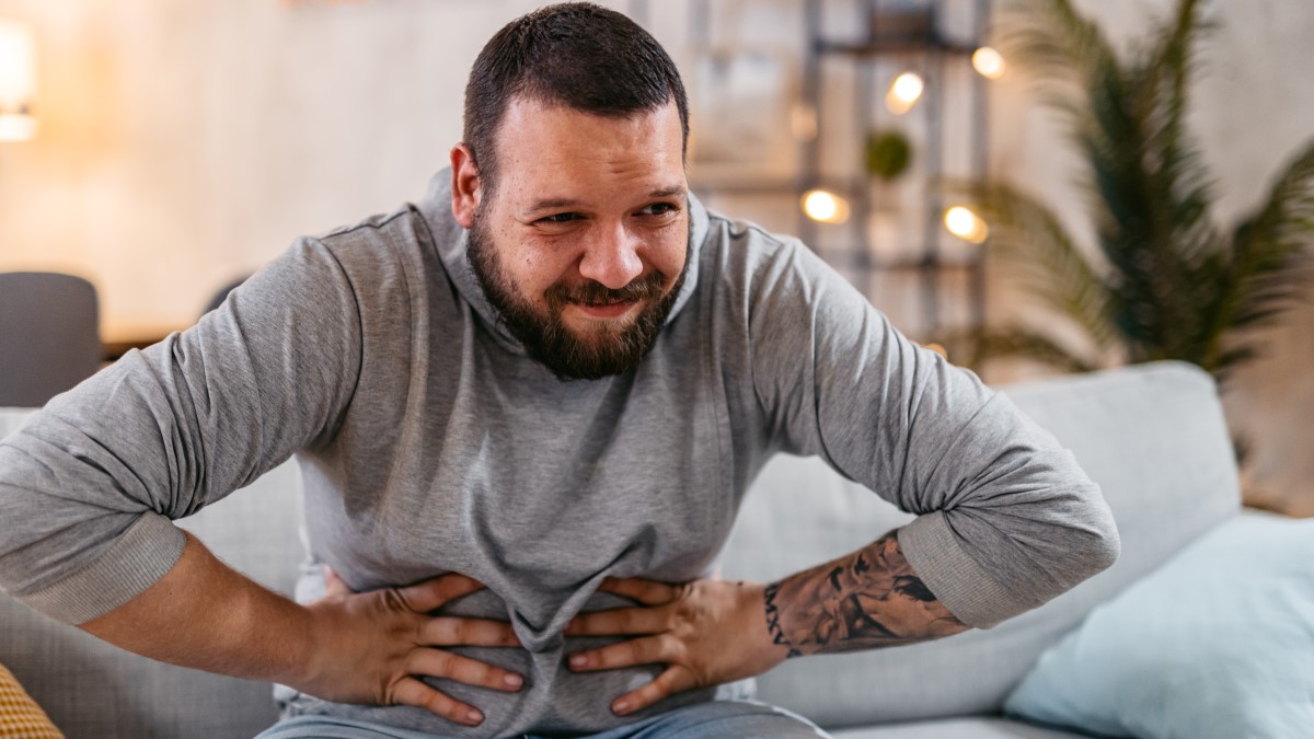 Man with stomach pain Man with a pained expression sitting on a couch clutching his stomach with both hands