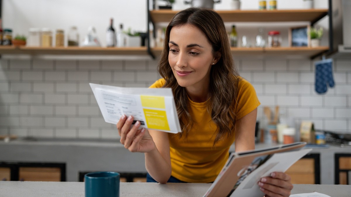Person reviewing report Woman in her kitchen holding mail and looking at a document.