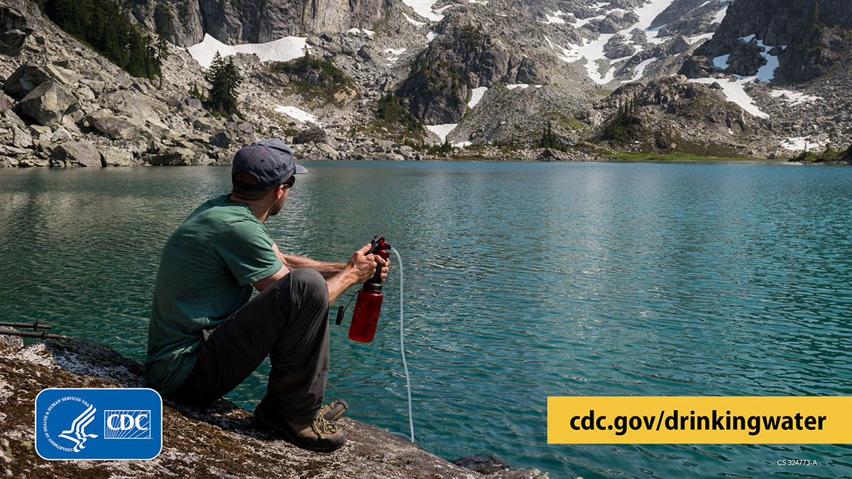 Filtering water from a mountain lake Hiker sitting next to a clear mountain lake and using a filter to treat water from the lake.