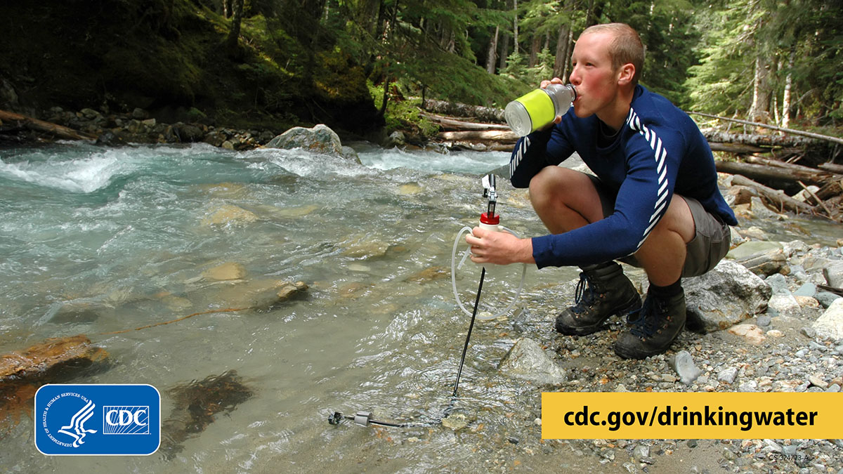 Filtering water from stream graphic 1200x675 Hiker holding a water filter in a mountain stream in one hand and drinking out of a water bottle with the other hand.