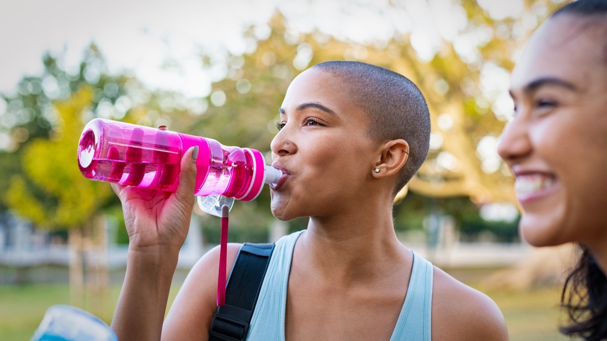 Drinking from water bottle Smiling woman outside drinking water out of a reusable water bottle next to another smiling woman