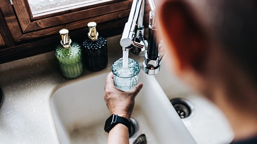 — title missing — Person filling up a glass with tap water from a kitchen faucet.