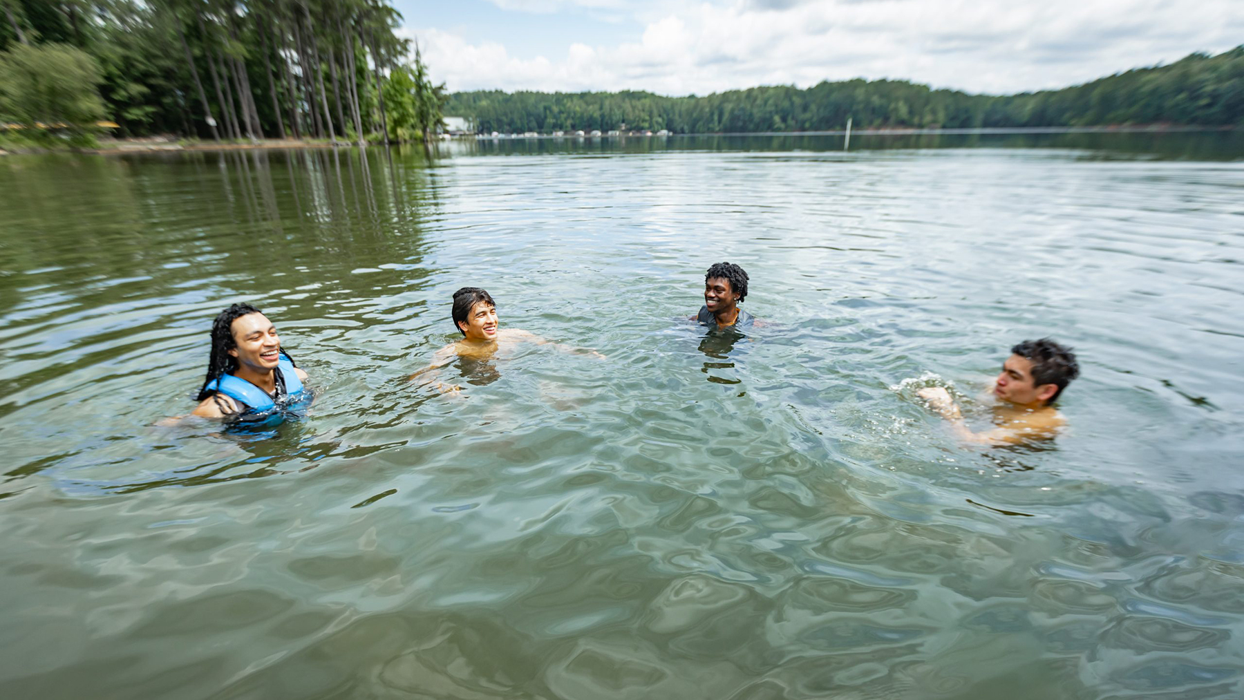 -- title missing -- Young men swimming safely together in a lake. Some have life jackets on.