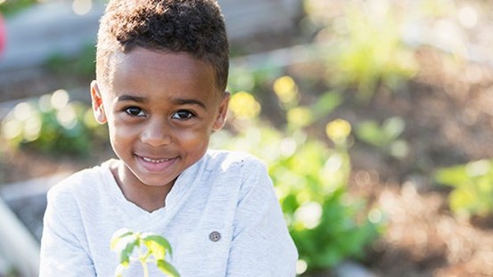 — title missing — Child smiling and holding a plant