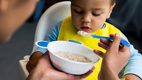 — title missing — Young child being fed from a bowl.