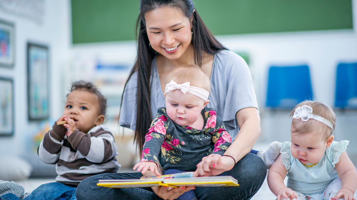 Early care educator sits with three young children Early care educator sits with three young children
