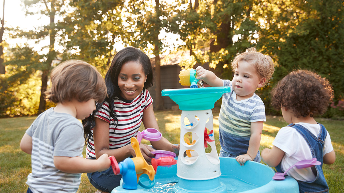 Teacher and young children Teacher kneels down to supervise young children while they play with water outdoors.