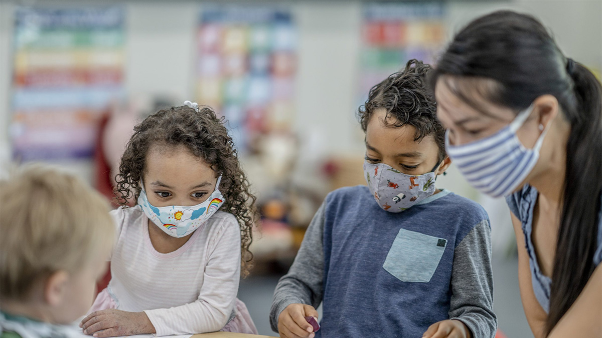 Teacher students with mask Teacher and young students wearing masks while they sit at a table together.