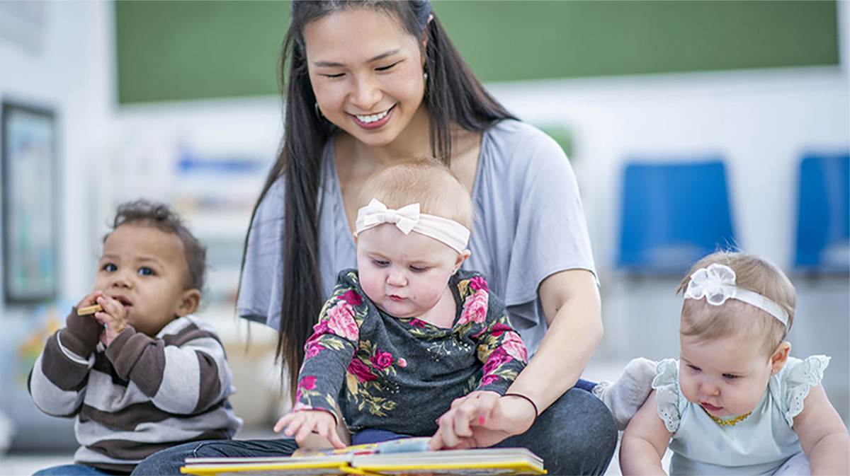 Teacher with toddlers Early educator reading a book to three young children.